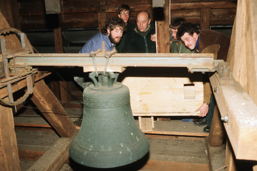 Anbringen eines Nistkastens in der Wiesenfelder Kirche Fünf Helfer heben gemeinsam einen großen Nistkasten an, im Vordergrund hängt eine Kirchenglocke.