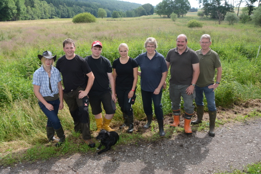 Ann-Christin Boland, Fabian, Sebastian und Wolfgang Kahler mit Ehefrau sowie Klaus Klimaschka stehen auf einem Weg vor der mit Gras bewachsenen Feuchtwiese, im Hintergrund sind einzelne kleinere Weiden, Bäume und der Waldrand zu sehen.